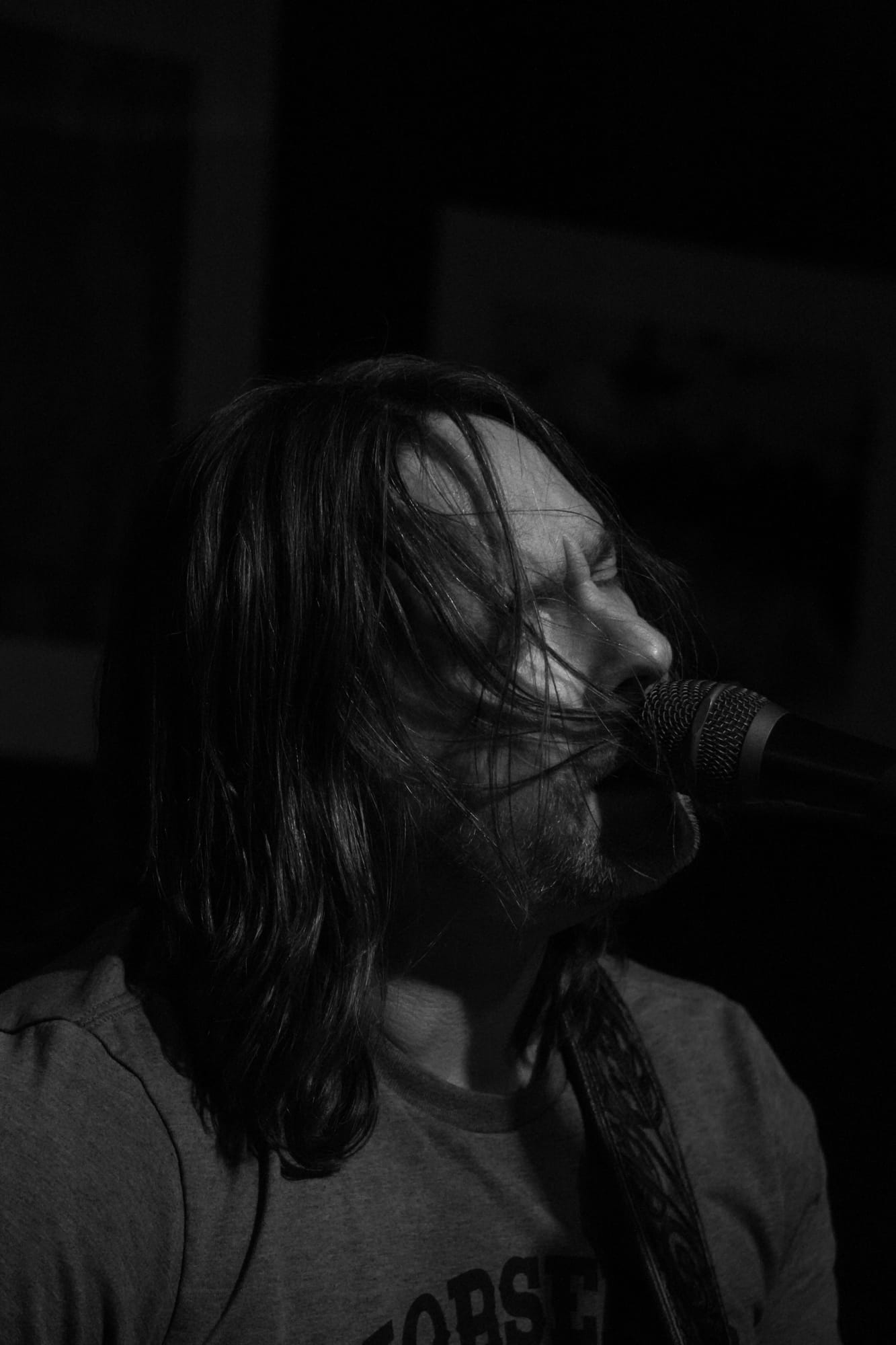 Black and white shot of a singer at a microphone, eyes closed and hair falling across their face mid-performance
